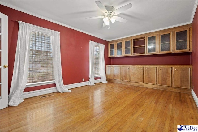 empty room featuring visible vents, baseboards, a ceiling fan, light wood-style flooring, and crown molding