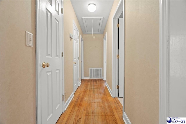 corridor with attic access, visible vents, light wood-style flooring, and baseboards