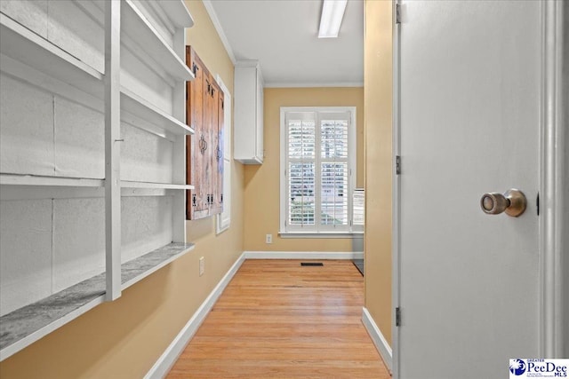 interior space featuring baseboards, light wood-type flooring, visible vents, and crown molding