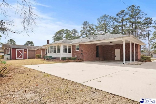 back of house featuring brick siding, a chimney, concrete driveway, and an outbuilding