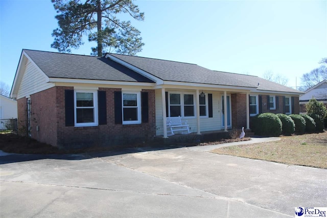 ranch-style home featuring covered porch, a shingled roof, and brick siding