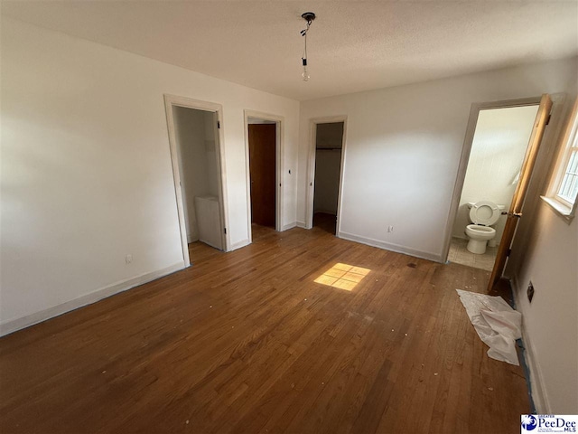 unfurnished bedroom with a textured ceiling, ensuite bath, wood finished floors, and baseboards