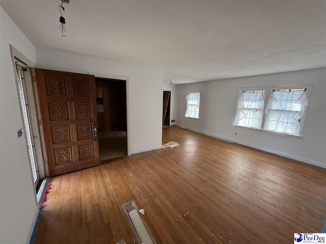 unfurnished room with a textured ceiling, wood finished floors, and baseboards