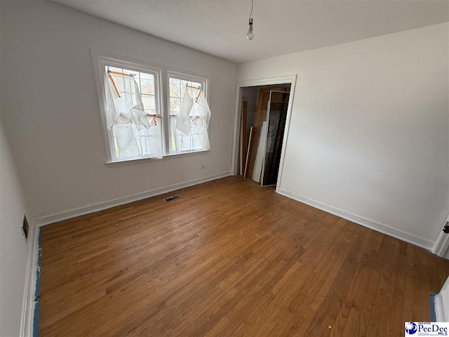 unfurnished room featuring wood finished floors, visible vents, and baseboards