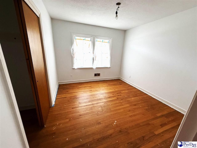 spare room featuring a textured ceiling, wood finished floors, and baseboards