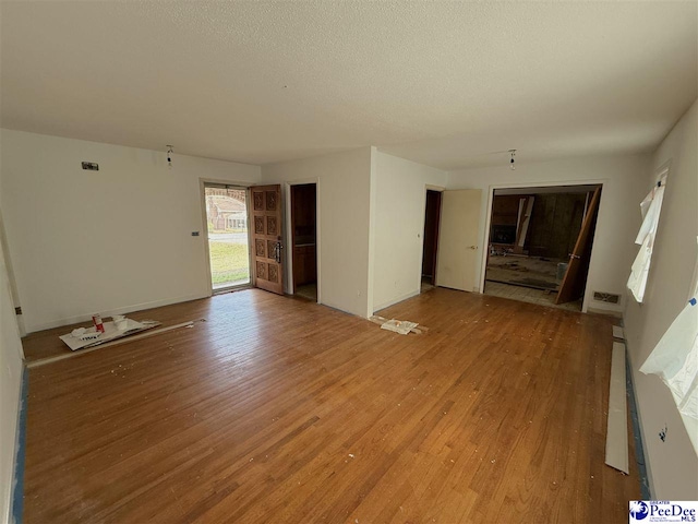 unfurnished living room featuring light wood-type flooring, a textured ceiling, and baseboards