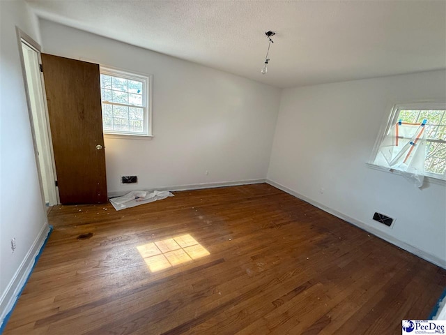 spare room with hardwood / wood-style flooring, visible vents, baseboards, and a textured ceiling