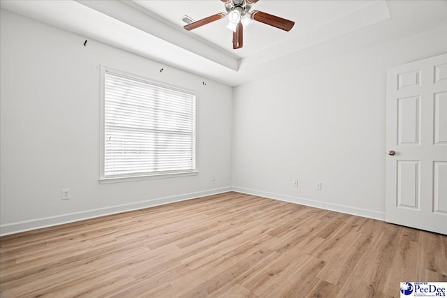 spare room with baseboards, a raised ceiling, a ceiling fan, and light wood-style floors