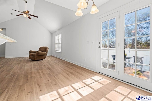 living area featuring vaulted ceiling, light wood finished floors, ceiling fan with notable chandelier, and baseboards