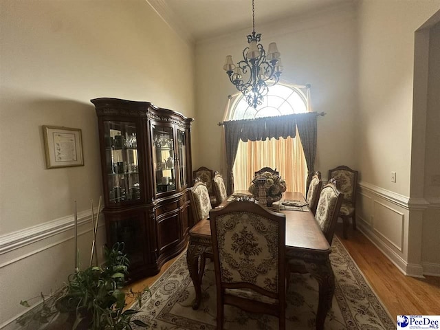 dining area featuring a wainscoted wall, a decorative wall, an inviting chandelier, ornamental molding, and wood finished floors