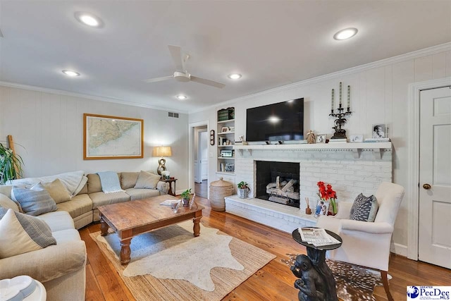 living room with wood-type flooring, ceiling fan, a fireplace, and crown molding