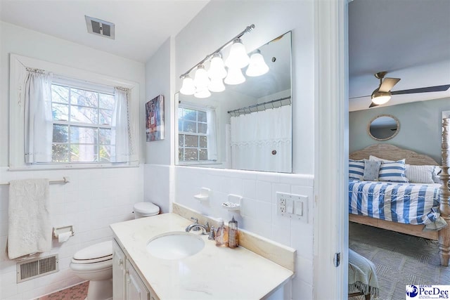 bathroom with ceiling fan, vanity, toilet, and tile walls