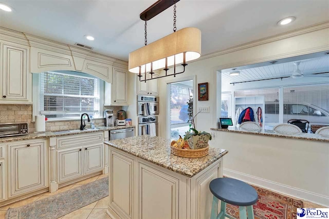 kitchen featuring sink, pendant lighting, light stone countertops, cream cabinets, and decorative backsplash