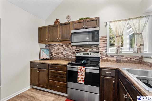 kitchen with lofted ceiling, backsplash, dark brown cabinets, stainless steel appliances, and light hardwood / wood-style floors