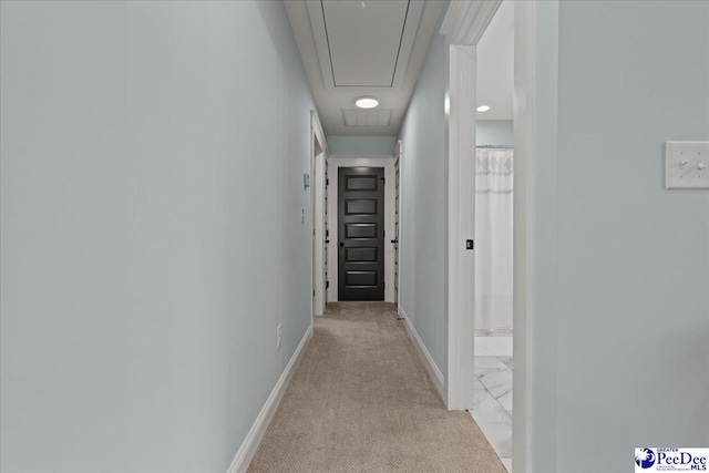 corridor with light colored carpet, attic access, and baseboards