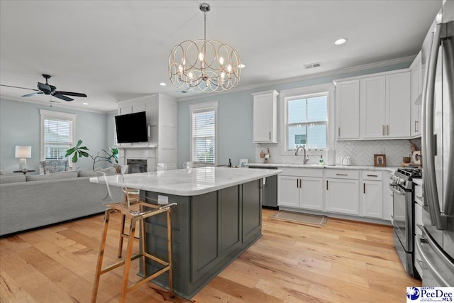 kitchen with crown molding, a sink, appliances with stainless steel finishes, white cabinetry, and open floor plan