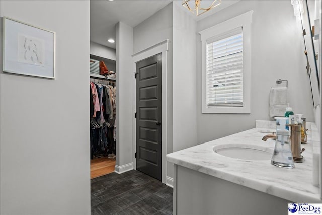 bathroom with baseboards, vanity, a walk in closet, and recessed lighting