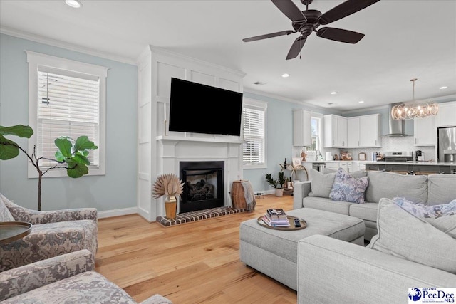 living room featuring ornamental molding, light wood-type flooring, recessed lighting, baseboards, and a glass covered fireplace