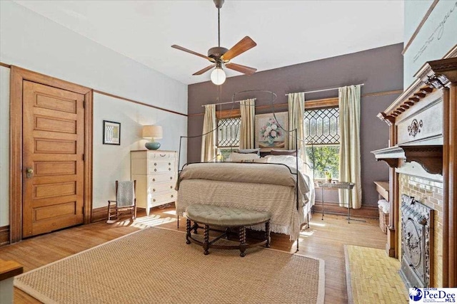 bedroom featuring a brick fireplace, ceiling fan, and light hardwood / wood-style flooring