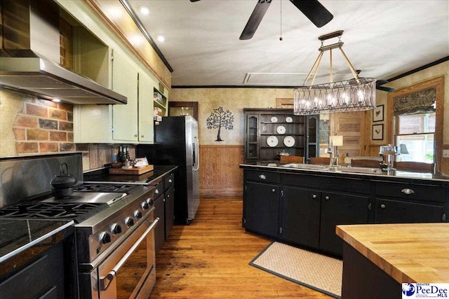 kitchen featuring crown molding, wall chimney range hood, decorative light fixtures, and stainless steel appliances