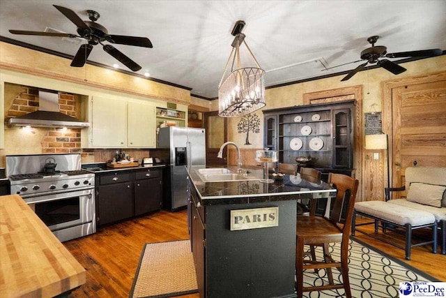 kitchen with wall chimney range hood, sink, a breakfast bar, stainless steel appliances, and a center island with sink