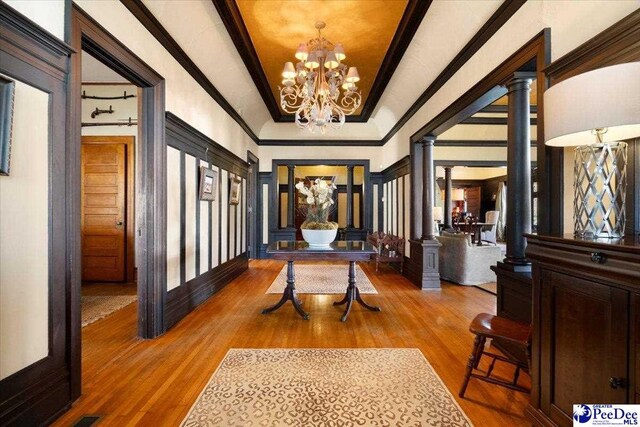 hall featuring an inviting chandelier, wood-type flooring, ornamental molding, and ornate columns