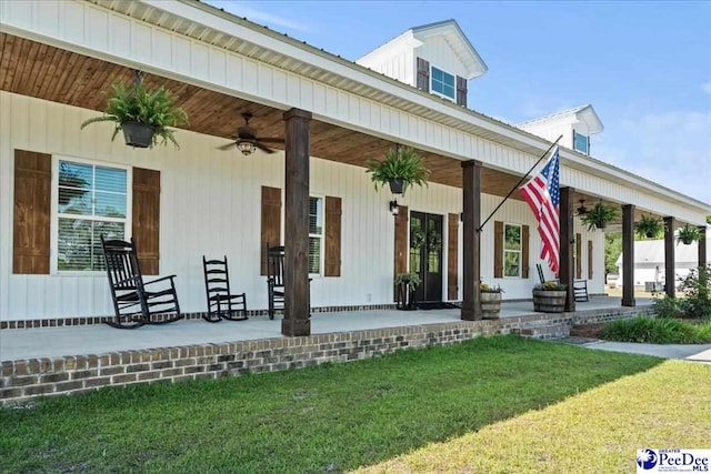 doorway to property featuring covered porch, ceiling fan, and a yard