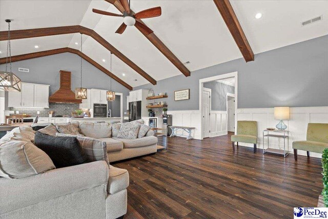 living area with visible vents, beam ceiling, a wainscoted wall, dark wood finished floors, and ceiling fan with notable chandelier