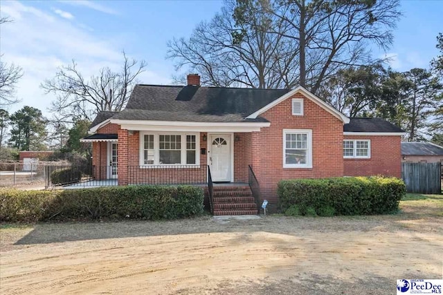 view of front of house featuring brick siding, fence, and a chimney