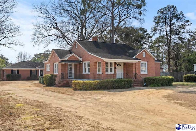 view of front of home with dirt driveway, a chimney, fence, and brick siding