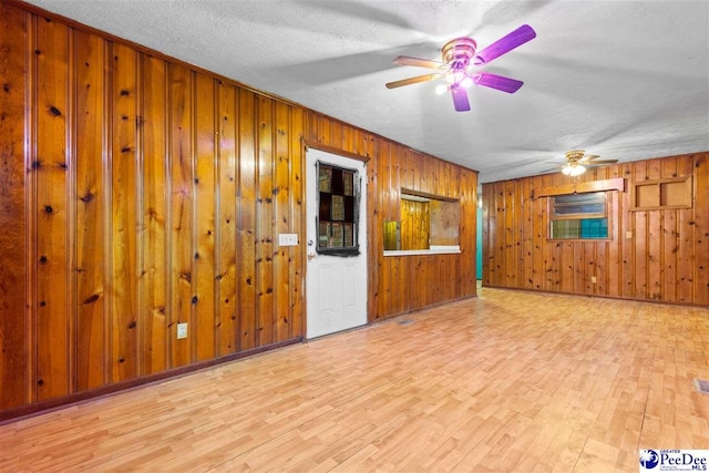 unfurnished room featuring a textured ceiling, ceiling fan, wood finished floors, and wooden walls