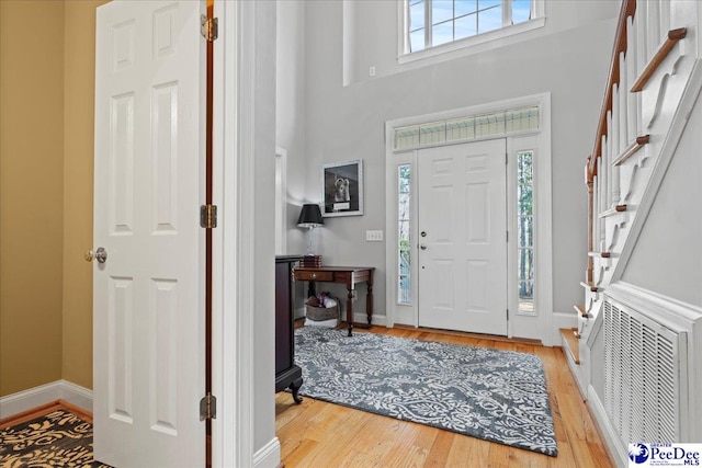 foyer entrance featuring light wood-style flooring, baseboards, visible vents, and a towering ceiling