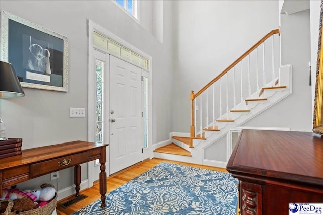 entrance foyer with visible vents, wood finished floors, stairway, a high ceiling, and baseboards