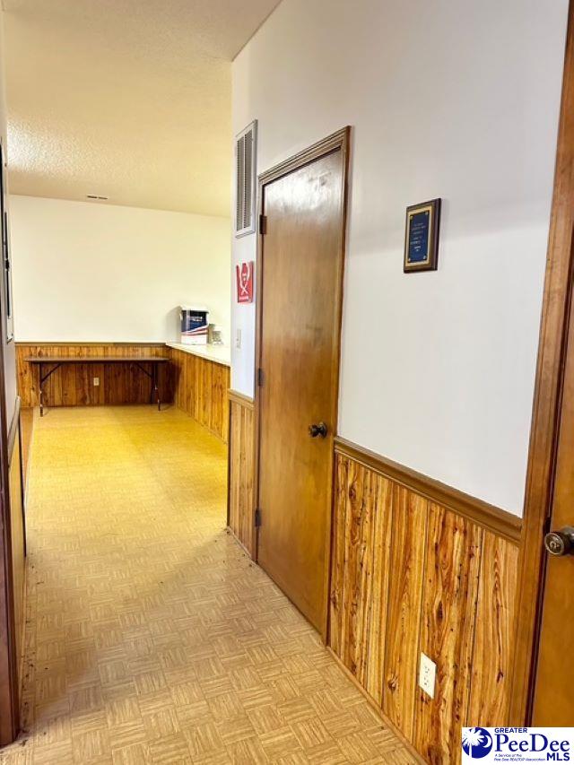 corridor featuring wainscoting, wood walls, visible vents, and a textured ceiling