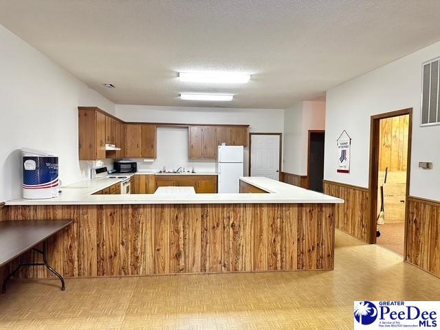 kitchen with a peninsula, white appliances, light countertops, wainscoting, and brown cabinets