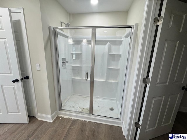 full bathroom featuring baseboards, wood finished floors, and a stall shower