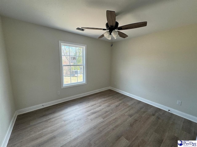 unfurnished room with a ceiling fan, baseboards, and dark wood-type flooring
