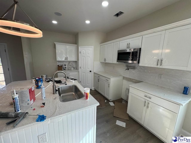 kitchen with a sink, stainless steel microwave, tasteful backsplash, white cabinetry, and dark wood-type flooring