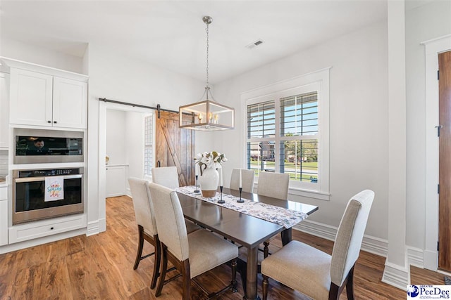 dining space with light wood-type flooring, baseboards, a barn door, and visible vents