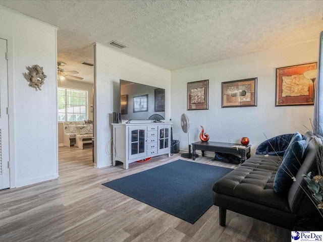 living room with ceiling fan, wood-type flooring, and a textured ceiling