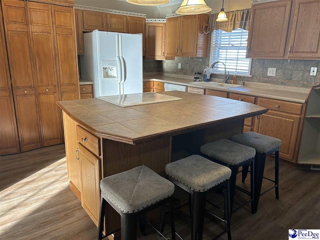 kitchen featuring a breakfast bar, dark wood-style flooring, tile counters, a sink, and white appliances