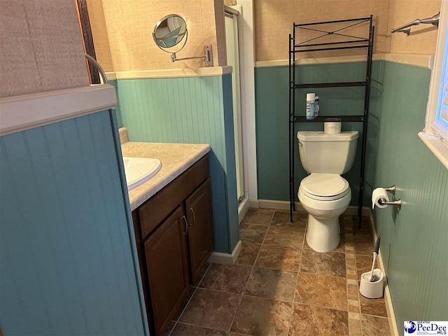 bathroom featuring stone finish flooring, a shower stall, toilet, and vanity