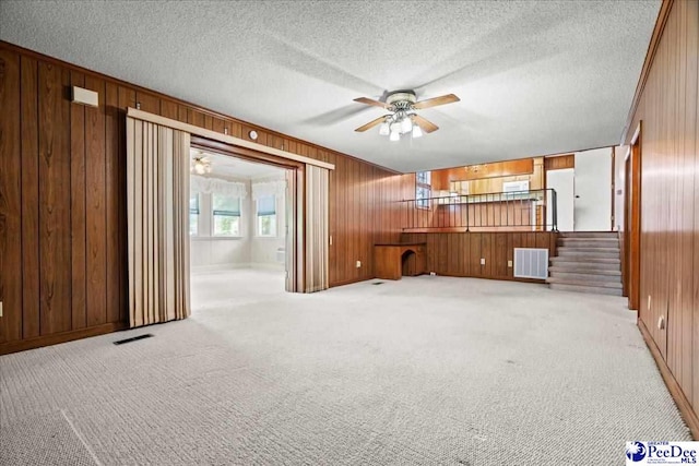 231 Timberlake Dr, Florence, SC 29501 - unfurnished living room with wooden walls, a ceiling fan, light carpet, stairs, and a textured ceiling