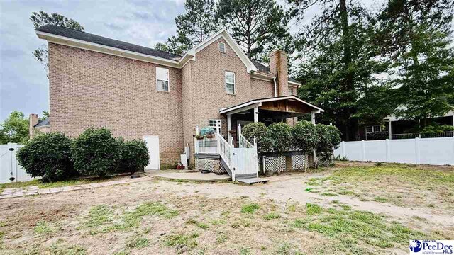 2423 Ben Hogan Cir, Florence, SC 29506 - rear view of house featuring a chimney, fence, brick siding, and a deck
