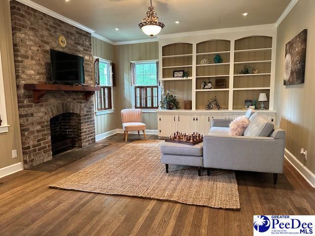 living room featuring wood-type flooring, crown molding, built in features, and a fireplace