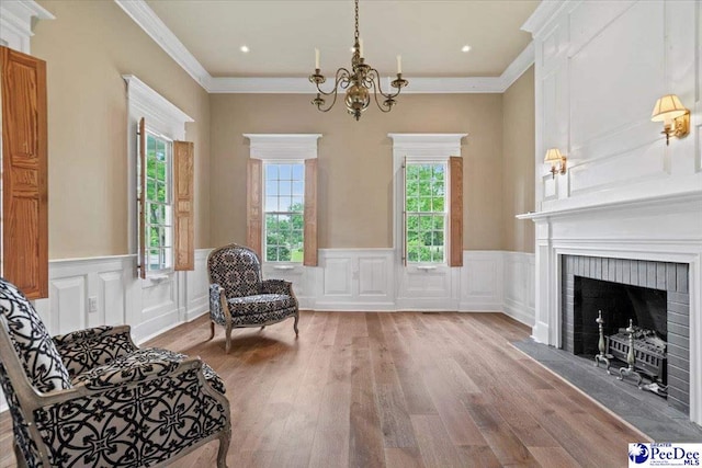 sitting room with an inviting chandelier, a fireplace, crown molding, and light hardwood / wood-style flooring