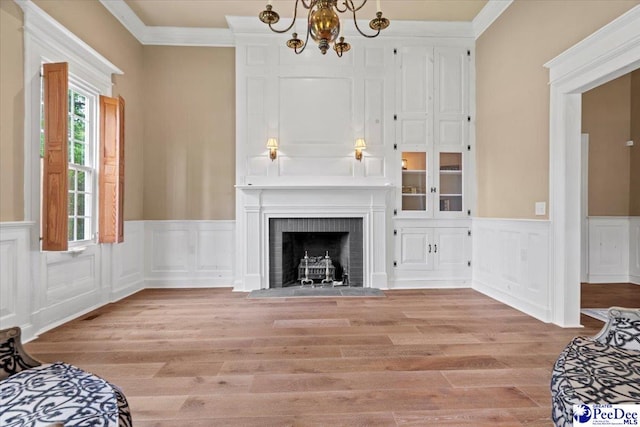 living room with an inviting chandelier, a brick fireplace, crown molding, and light hardwood / wood-style floors