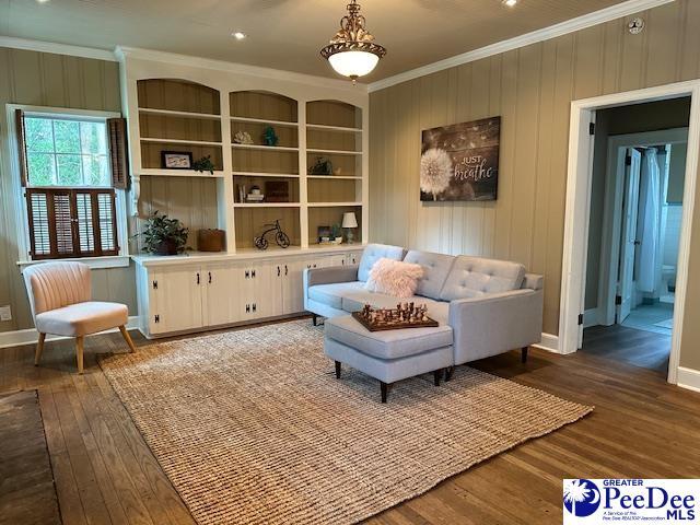 sitting room featuring wooden walls, ornamental molding, dark hardwood / wood-style floors, and built in features