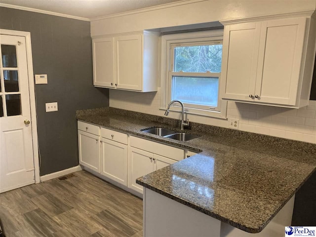 kitchen featuring sink, white cabinets, decorative backsplash, dark stone counters, and crown molding