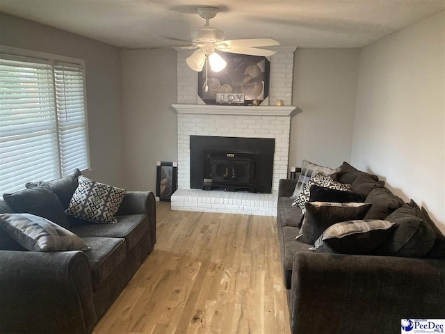 living room with ceiling fan, a brick fireplace, and light hardwood / wood-style floors